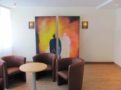 În prim-plan sunt trei scaune individuale din piele, iar în fundal o imagine cu două figuri abstracte în alb și negru.