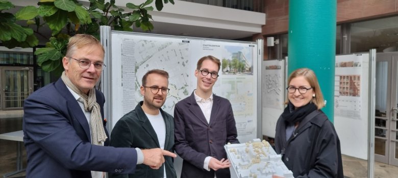 Soldan Marcus Hille (jüri başkanı), Valentin Martin, Fabian Wieczorek ve Pauline Rohländer (ROHWAREIMSTUDIO'dan) olmak üzere dört kişi, kazanan modelin yer aldığı tasarımın mimari planlarının önünde durmaktadır.