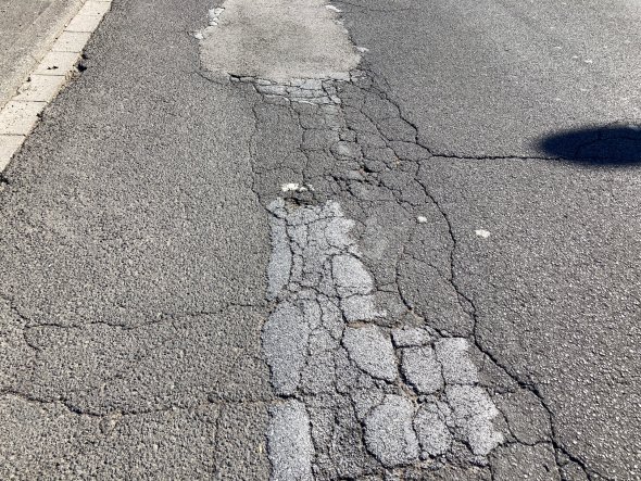 Wilhelm-Leuschner-Straße'de yol işaretleri solmuş, ağır hasar görmüş ve çatlamış bir yol bölümünün yakın çekimi