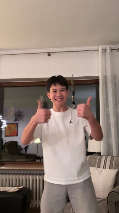 Tim Kolberg Genç bir adam pencerenin önünde duruyor ve iki başparmağını da yukarı doğru uzatıyor