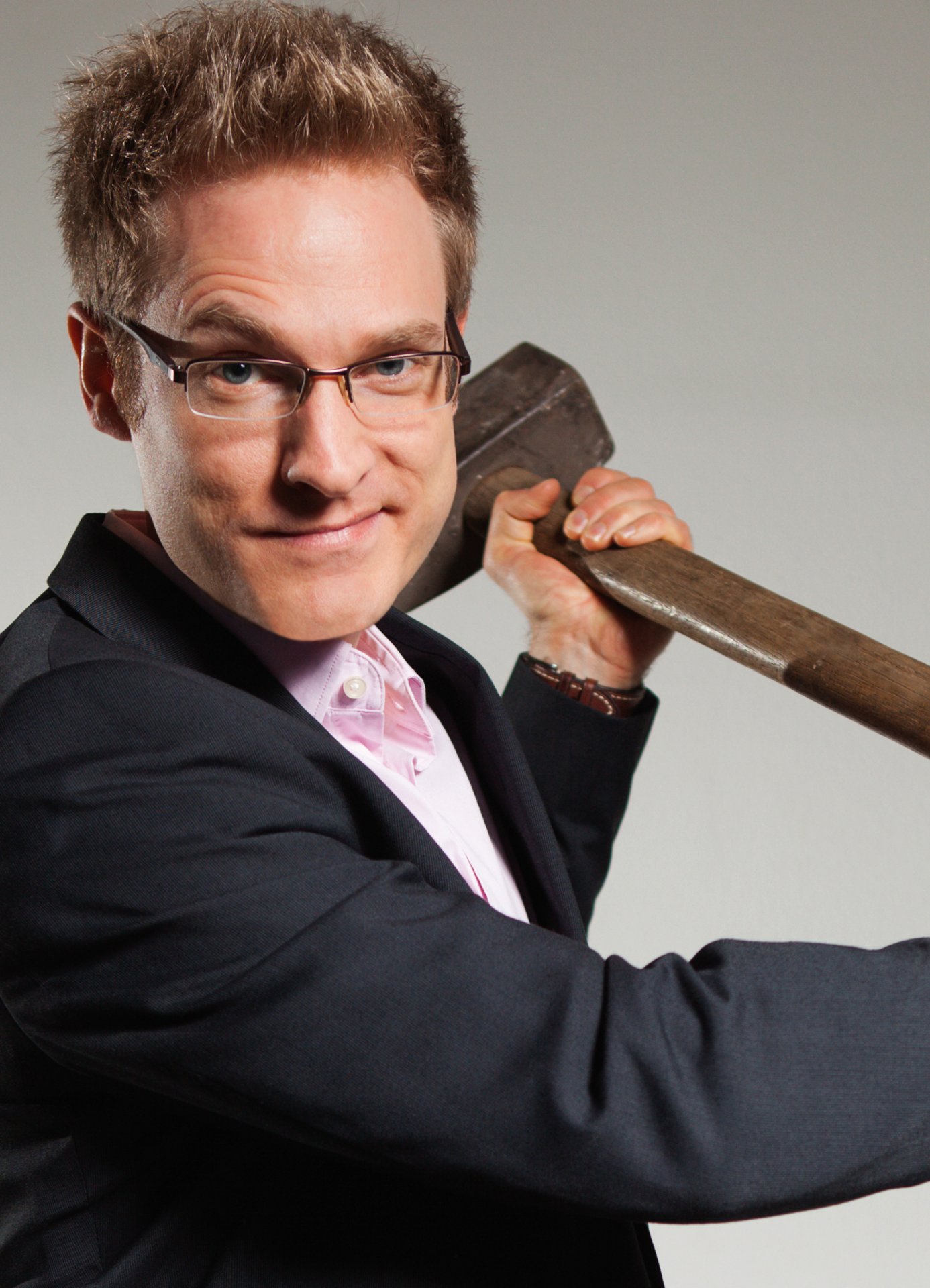 Людина з коротким світлим волоссям у чорному костюмі та світло-рожевій сорочці, з важкою сокирою через плече