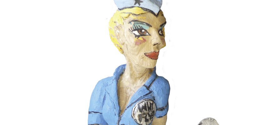 Skulptur eines sitzenden Piloten in blauer Uniform, auf einem Flugzeug. Material: Roteiche, Höhe ca. 60 cm, Jahr: 2019. Beschriftung: 'Pop-A-Roc'.