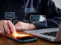 Chatbot-Wahl Eine Hand tippt auf ein Smartphone, daneben ist ein Laptop zu sehen. Virtuell ist eine Sprechblase zu sehen mit dem Begriff "Chatbot".