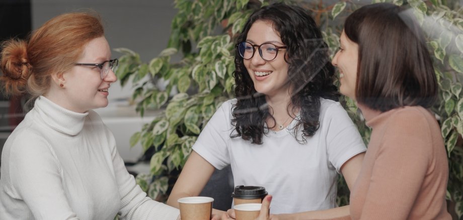 three female friends are talking in a coffee shop and drinking tea, moral support and caring friendship. mental health