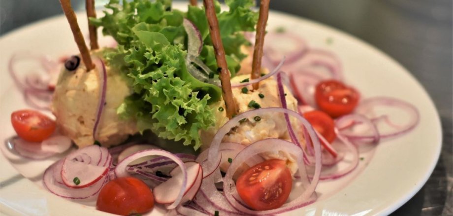 Zwei Kugeln Obatzter mit Brezelstangen auf einem Teller, umgeben von roten Zwiebelringen, halbierten Kirschtomaten und Salatblättern