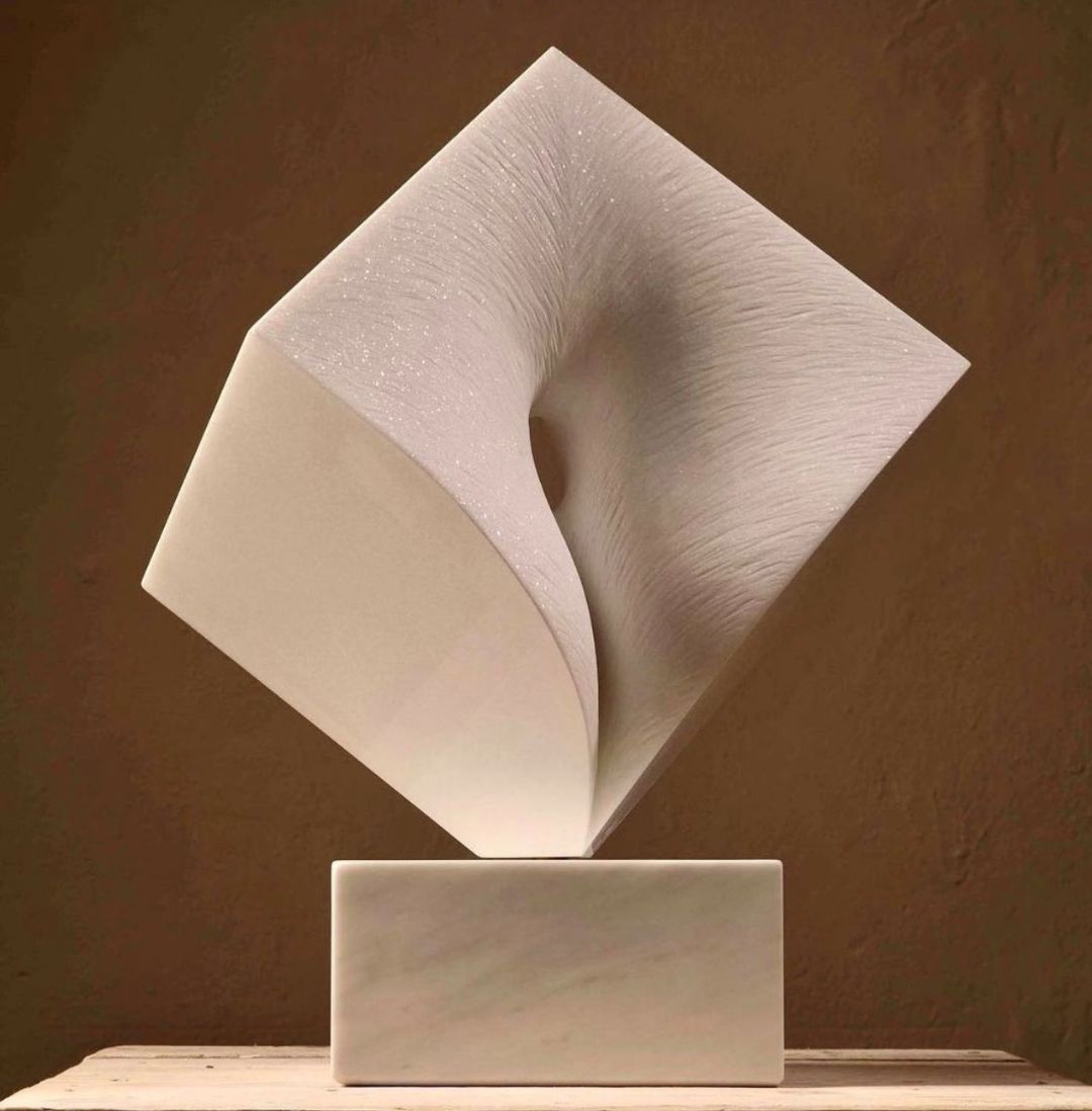Abstrakte Skulptur aus hellem Material mit einer verdrehten, konkaven Form auf einem rechteckigen Sockel