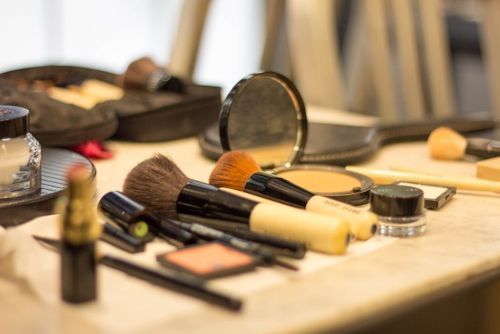 Make-up-Pinsel, Lippenstift, Puderkompakt und weitere Kosmetikprodukte auf einem Tisch arrangiert