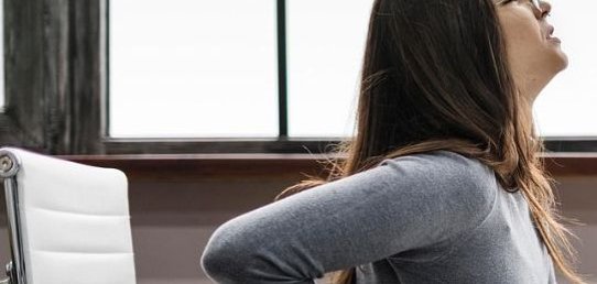 Zwei Frauen in Sportkleidung. Die Frau links trägt ein schwarzes T-Shirt und eine Leggings mit lila Muster. Die Frau rechts trägt ein schwarzes Oberteil und schwarze Leggings, mit rosa Schuhen. Die linke Frau unterstützt die rechte, die in einer sportlichen Pose steht.