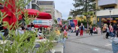 Puiseauxplatz Vor dem Eiscafe am Puiseauxplatz sitzen Menschen. Im Vordergrund sind Pflanzen und an der Seite Passanten.