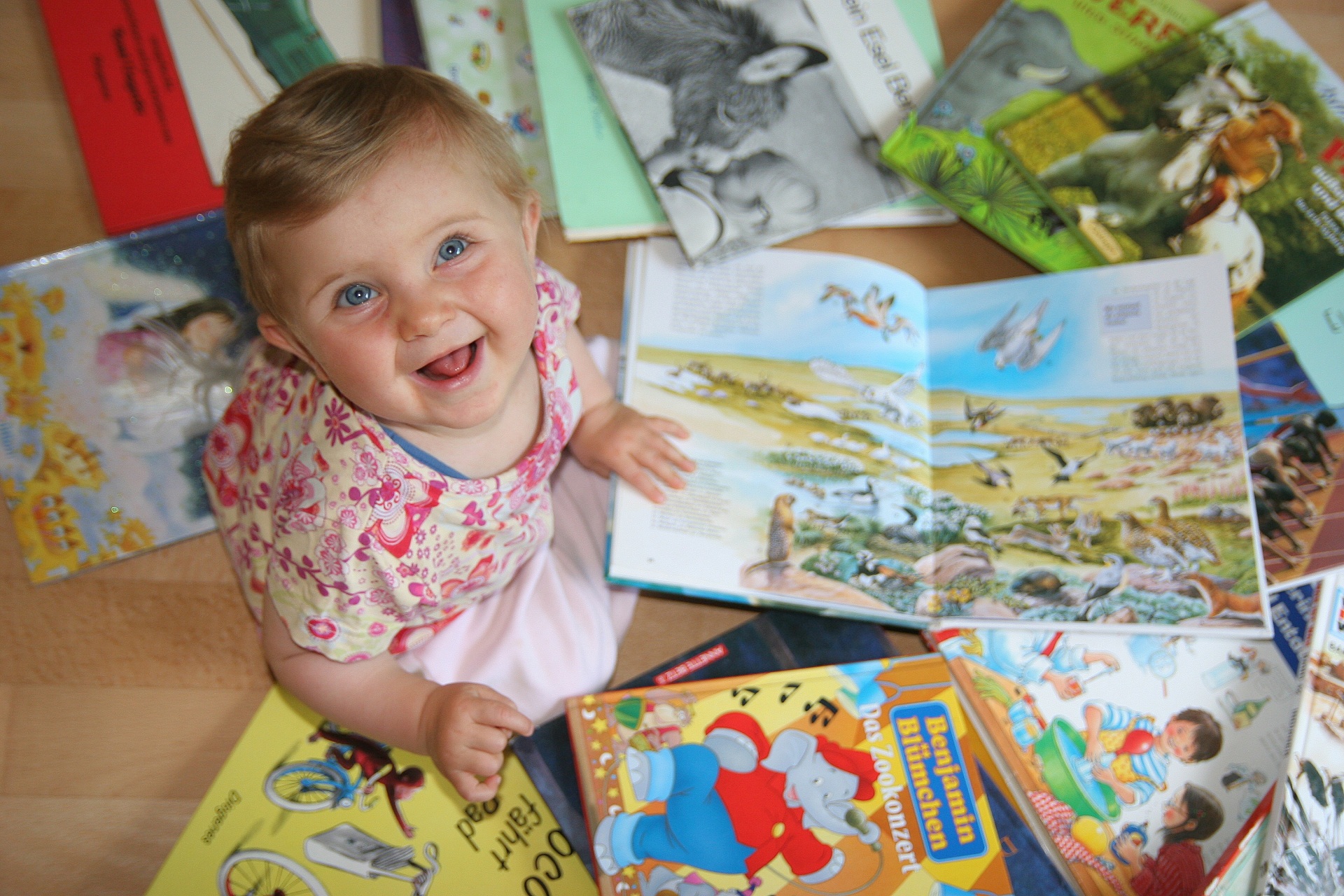 Kleinkind Kleines Kind sitzt auf dem Boden und schaut sich mehrere aufgeschlagene Kinderbücher mit bunten Illustrationen an