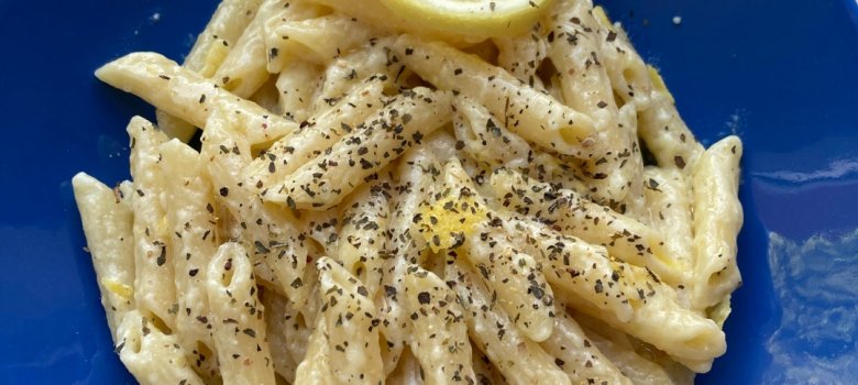 Das Bild zeigt einen blauen Teller mit Nudeln, angerichtet mit einer Zitronenscheibe.