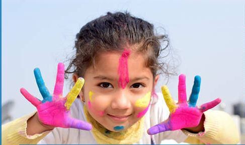 Kleines Mädchen Kind zeigt bunte, bemalte Hände mit Farben wie Blau, Pink, Gelb und Lila vor klarem Himmel