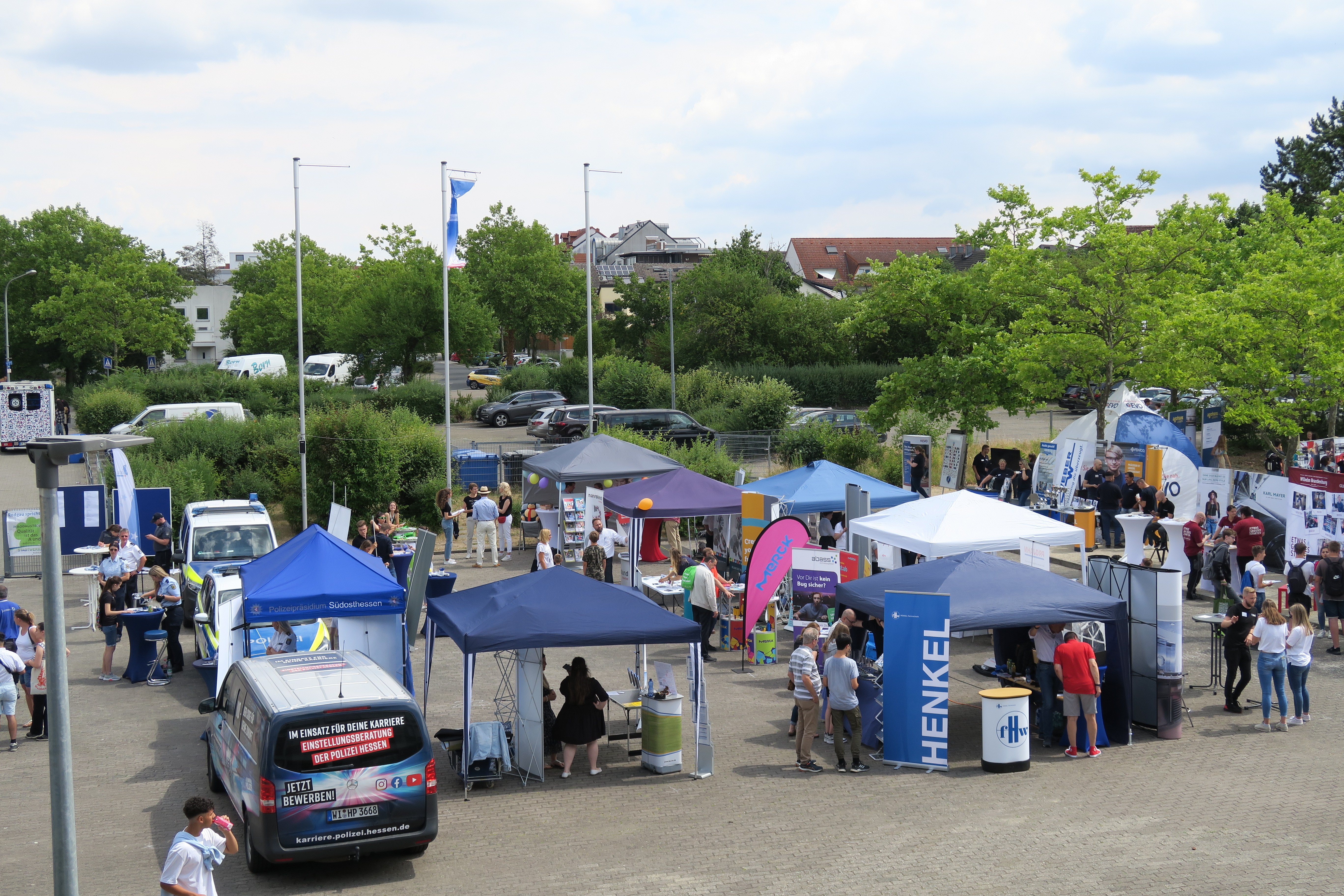 Bildungsmesse Außenbereich einer Bildungsmesse mit mehreren Ständen, Besuchern und einem Stand von Henkel unter blauem Himmel