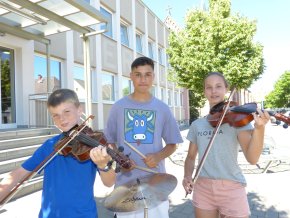 Musikschule Drei Schüler der Musikschule spielen draußen Instrumente: zwei mit Violinen, einer mit Schlagzeugstöcken vor einem Gebäude