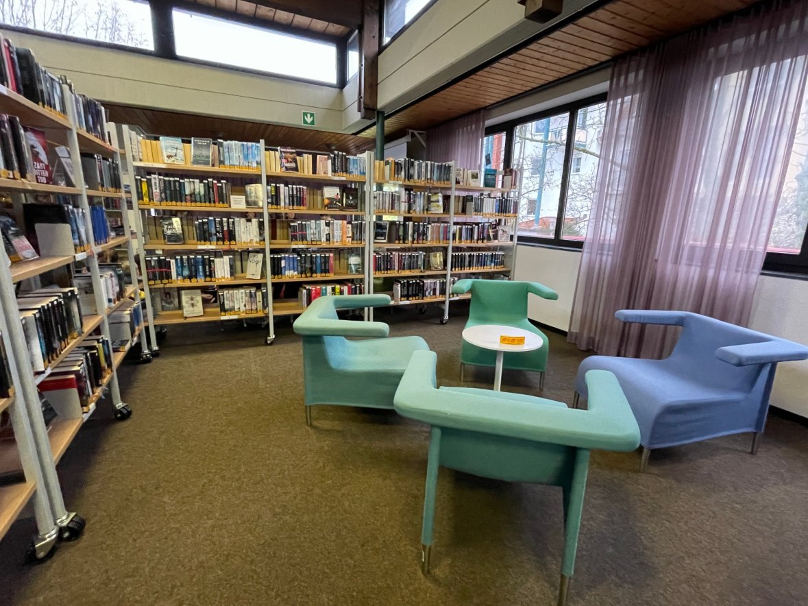 Stadtbücherei Niederroden Innenraum der Stadtbücherei Niederroden mit Bücherregalen und modernen Sitzmöbeln in Pastellfarben neben großen Fenstern
