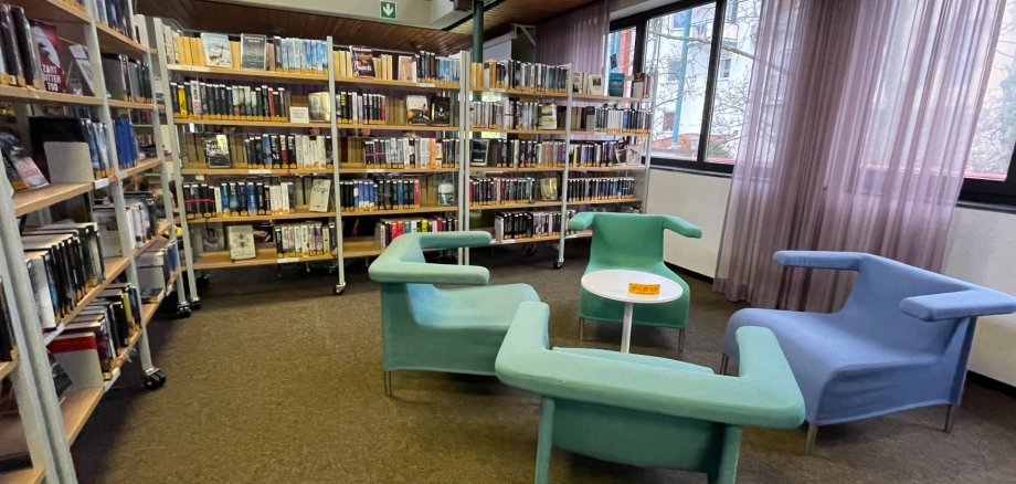 Innenraum der Stadtbücherei Niederroden mit Bücherregalen und modernen Sitzmöbeln in Pastellfarben neben großen Fenstern