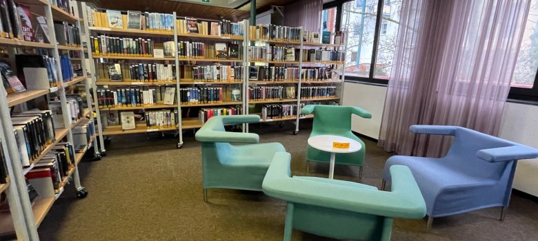 Stadtbücherei Niederroden Innenraum der Stadtbücherei Niederroden mit Bücherregalen und modernen Sitzmöbeln in Pastellfarben neben großen Fenstern