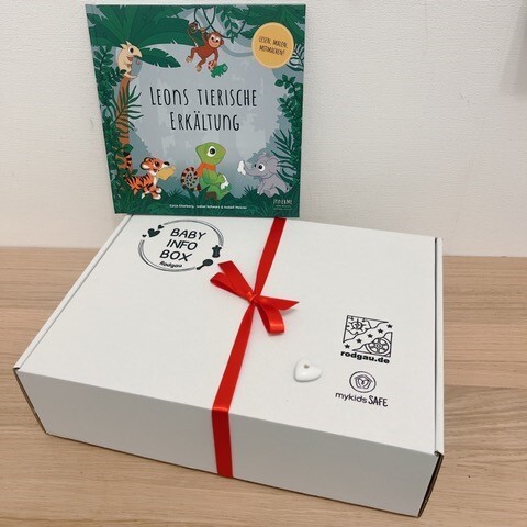 Weiße Baby Info Box mit rotem Band und Buch Weiße Baby Info Box mit rotem Band und Buch 'Leons tierische Erkältung' mit Tierillustrationen im Hintergrund