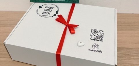 Weiße Baby Info Box mit rotem Band und Buch 'Leons tierische Erkältung' mit Tierillustrationen im Hintergrund