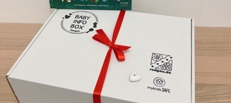 Weiße Baby Info Box mit rotem Band und Buch Weiße Baby Info Box mit rotem Band und Buch 'Leons tierische Erkältung' mit Tierillustrationen im Hintergrund
