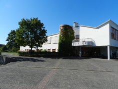 Blick auf den Eingangsbereich mit Schulhof und Gebäude sowie einem Baum