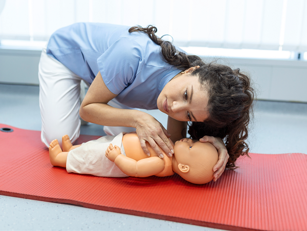 Person führt Mund-zu-Mund-Beatmung an Babypuppe auf roter Matte im Erste-Hilfe-Kurs durch