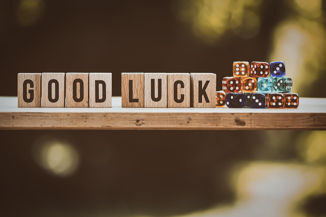 Good Luck Holzwürfel mit den Buchstaben 'GOOD LUCK' neben einem Stapel bunter Spielwürfel auf einem Holzbrett