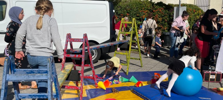 Kinder spielen auf einem bunten Spielplatz Kinder spielen auf einem bunten Spielplatz mit Leitern, Matten und einem großen blauen Gymnastikball bei einem Fest im Freien