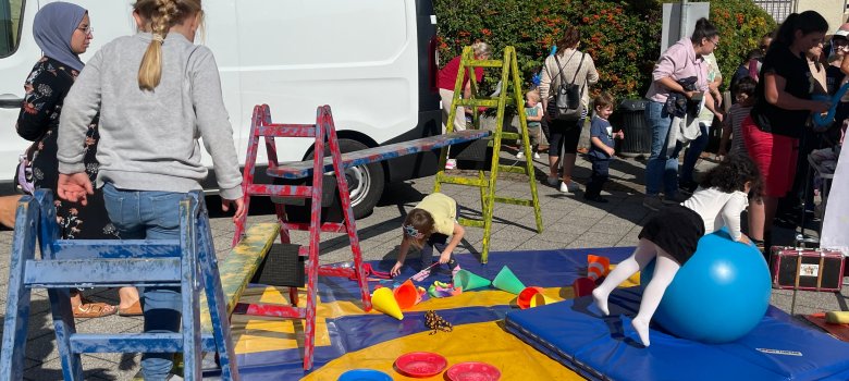 Kinder spielen auf einem bunten Spielplatz Kinder spielen auf einem bunten Spielplatz mit Leitern, Matten und einem großen blauen Gymnastikball bei einem Fest im Freien
