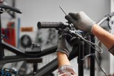 Mann mit Handschuhen justiert mit einem Werkzeug die Bremsen an einem Fahrradlenker.