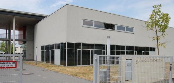 Moderne Aula der GBS mit großen Glasfenstern, flachem Dach und einem Eingang mit überdachtem Bereich