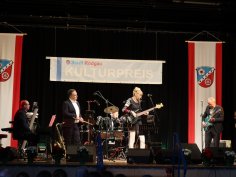 Kulturpreis-Verleihung Band spielt auf Bühne bei der Kulturpreis-Verleihung der Stadt Rodgau mit Banner und zwei roten Fahnen mit Wappen