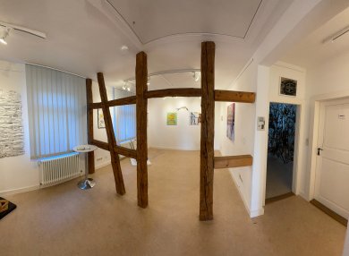 Innenraum der Rodgau Galerie mit weißen Wänden, mehreren Kunstwerken an den Wänden und einer hölzernen Fachwerkstruktur in der Mitte