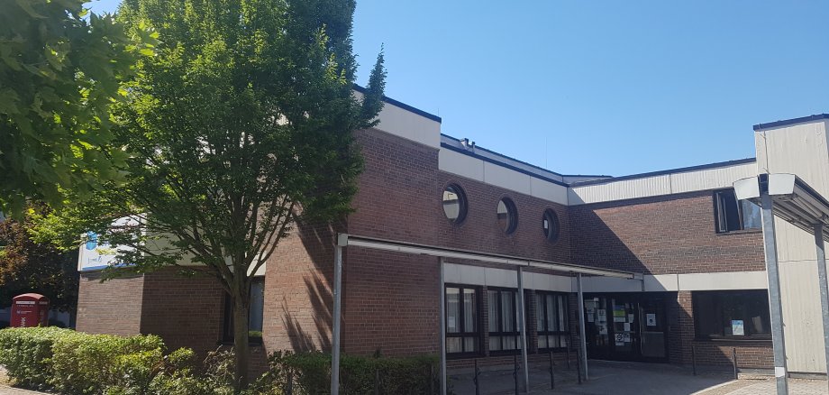 Eingangsbereich des Sozialzentrums Niederroden mit Backsteinfassade, mehreren runden Fenstern und Bäumen im Vordergrund