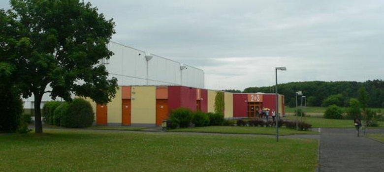 Sporthalle Dudenhofen Im Vordergrund steht ein großer Baum, dahinter die Sporthalle Dudenhofen.