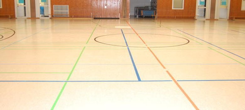 Sporthalle Innenansicht der Sporthalle Jügesheim, ausgestattet mit einem Basketballfeld und einer Bodenmarkierung.