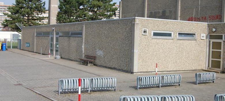 Sporthalle Außenansicht der Sporthalle Nieder-Roden, umgeben von einem Zaun und ausgestattet mit Fahrradständern.