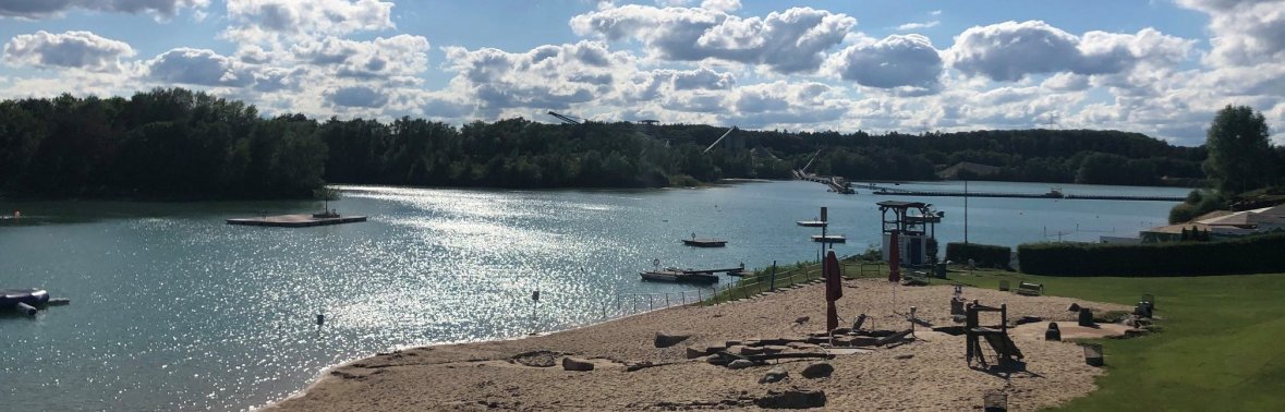 Ein Strand mit Booten und einem See im Hintergrund, umgeben von sanften Wellen und grünem Ufer.