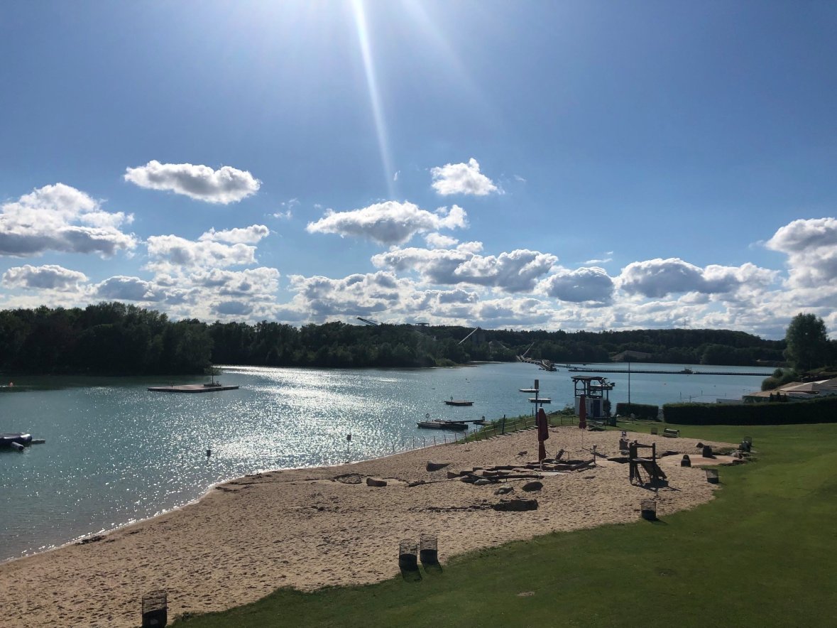 Strandbad Rodgau Ein Strand mit Booten und einem See im Hintergrund, umgeben von sanften Wellen und grünem Ufer.