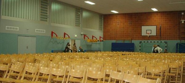Turnhalle Innenansicht der Turnhalle Carl-Orff-Schule mit vielen Holzstühlen in geordneten Reihen.