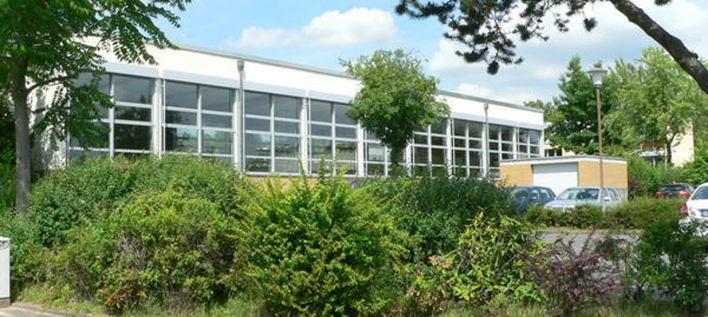 Turnhalle Ansicht der Turnhalle Freiherr-vom-Stein-Schule, umgeben von dichten Bäumen und bunten Sträuchern.