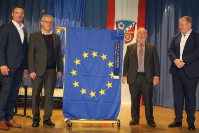 Bürgermeister Breitenbach, Stadtrat Schüssler und Stadtverordnetenvorsitzender Kaiser stehen auf einer Bühne; in der Mitte ist eine Europafahne