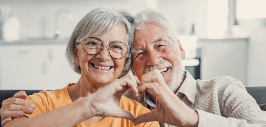 Eine ältere Dame und ein Herr halten ihre Hände gemeinsam zu einem Herz geformt.