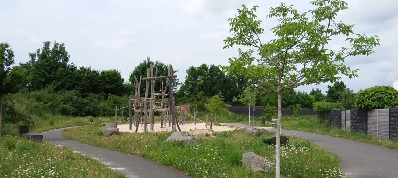 Helixpark Zwei Wege im Helixpark in Hainhausen schlängeln sich um einen Spielbereich herum. Rechts im Vordergrund steht ein junger Baum am Rand sind Wiese und Bäume.