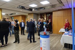 Personen versammeln sich um Tische in einem Bürgerhaus, dekoriert mit blauen und weißen Schildern