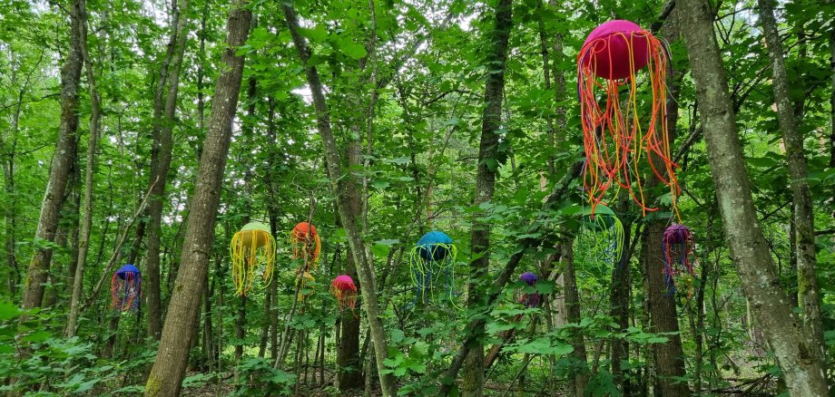 Grüner Wald in Nieder-Roden mit bunten Kunstwerken in den Bäumen