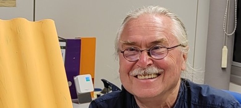 Winno Sahm Winno Sahm sitzt an einem Tisch in einem Büro mit Postern an der Wand und einem großen gelben Plakat vor sich