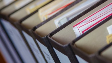 Acht gefüllte Aktenordner mit zahlreichen Dokumenten, von oben betrachtet.