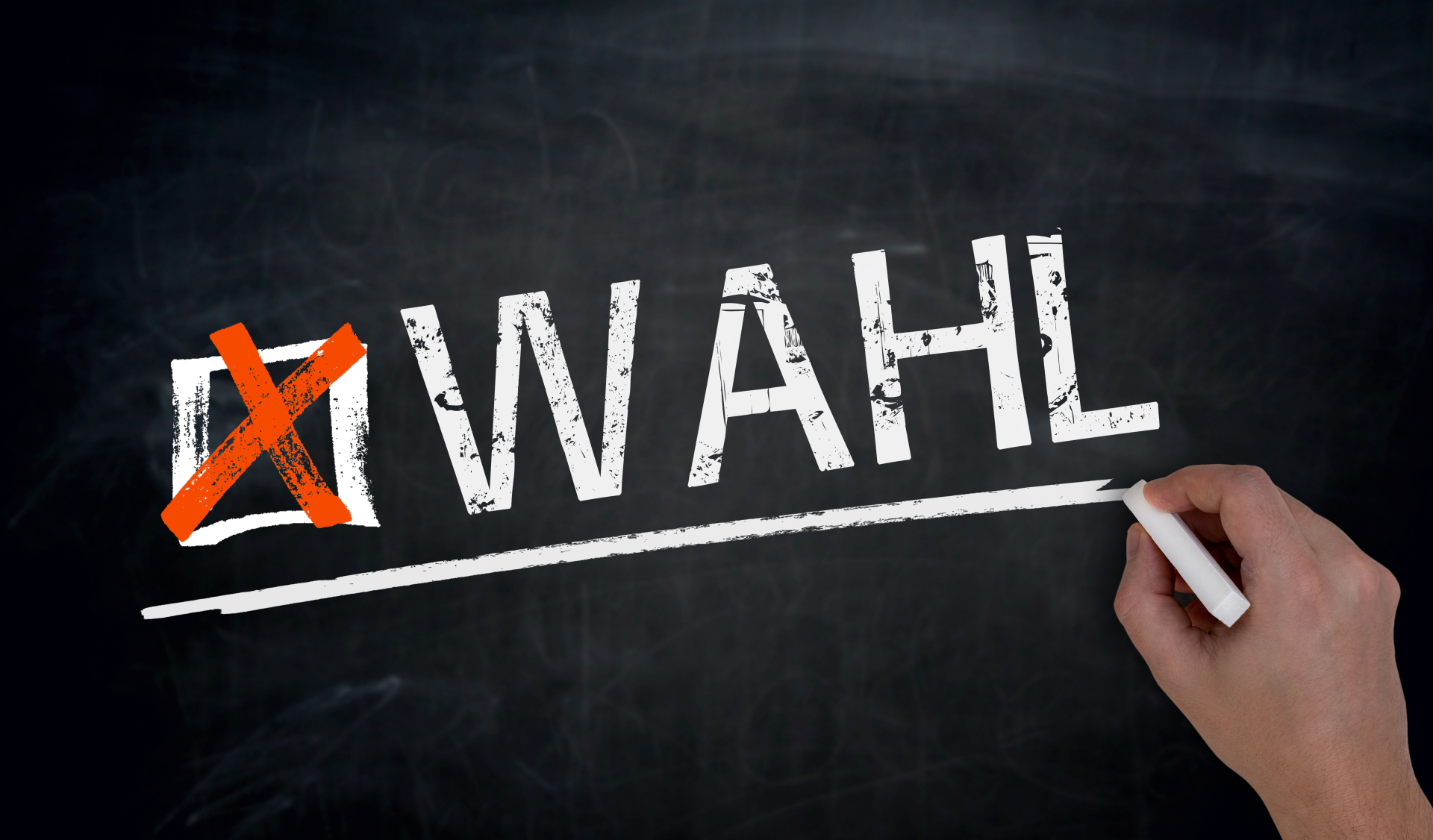 Wahl Hand schreibt mit weißer Kreide auf eine schwarze Tafel das Wort 'WAHL' mit einem roten Kreuz in einem Kästchen davor.