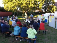 Bürgerbeteiligung Bürgerbeteiligung im Rodaupark mit etwa 20 Personen, die auf Bänken im Freien sitzen und einem Sprecher zuhören, der vor Pinnwänden mit Notizen steht.